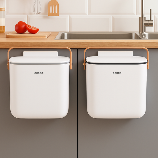 Two white compact trash bins (grey and black outline) with rolling lids, mounted on a wall above a gray countertop, with a sink and red peppers in the background.